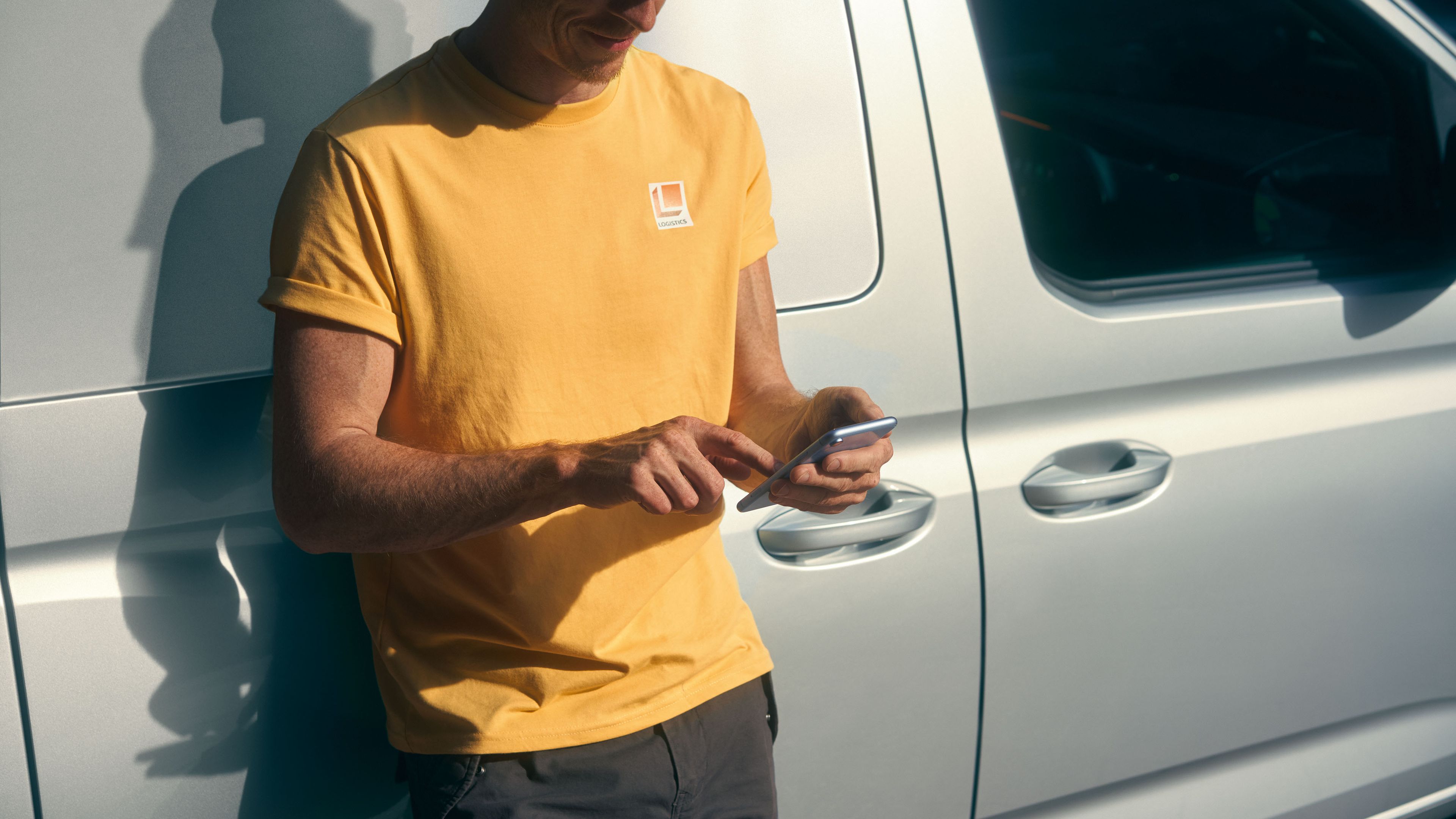Ein Mann lehnt an einem VW Caddy Cargo Maxi und bedient sein Smartphone.