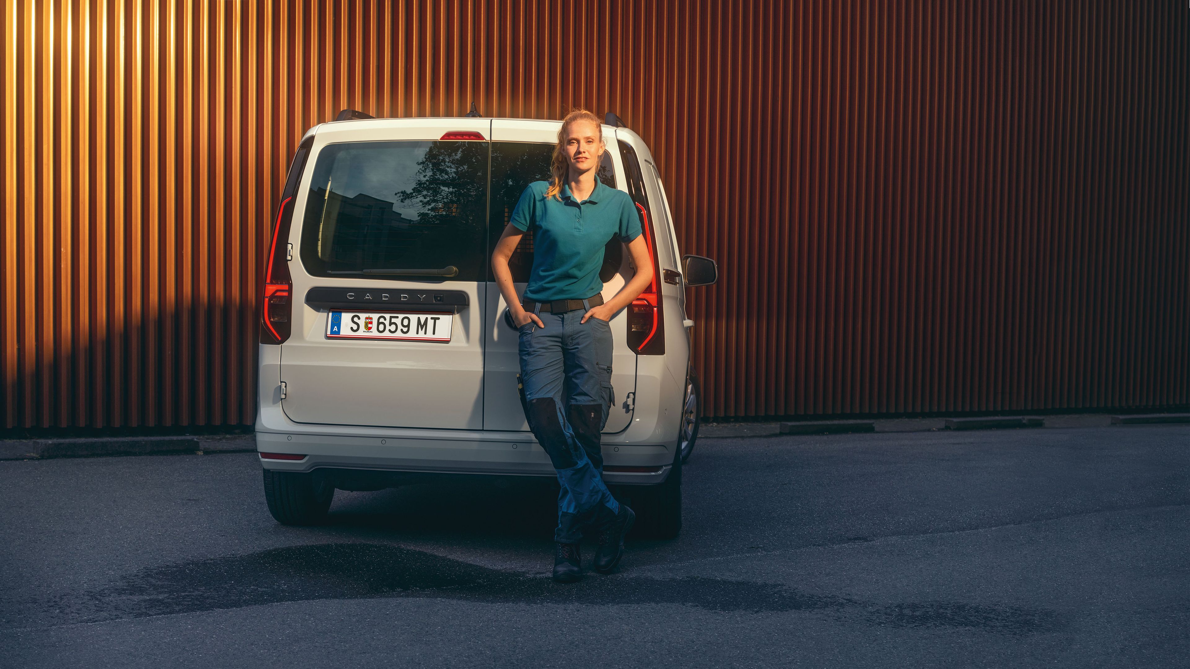 Eine Frau lehnt am Heck eines weißen VW Caddy Cargo.