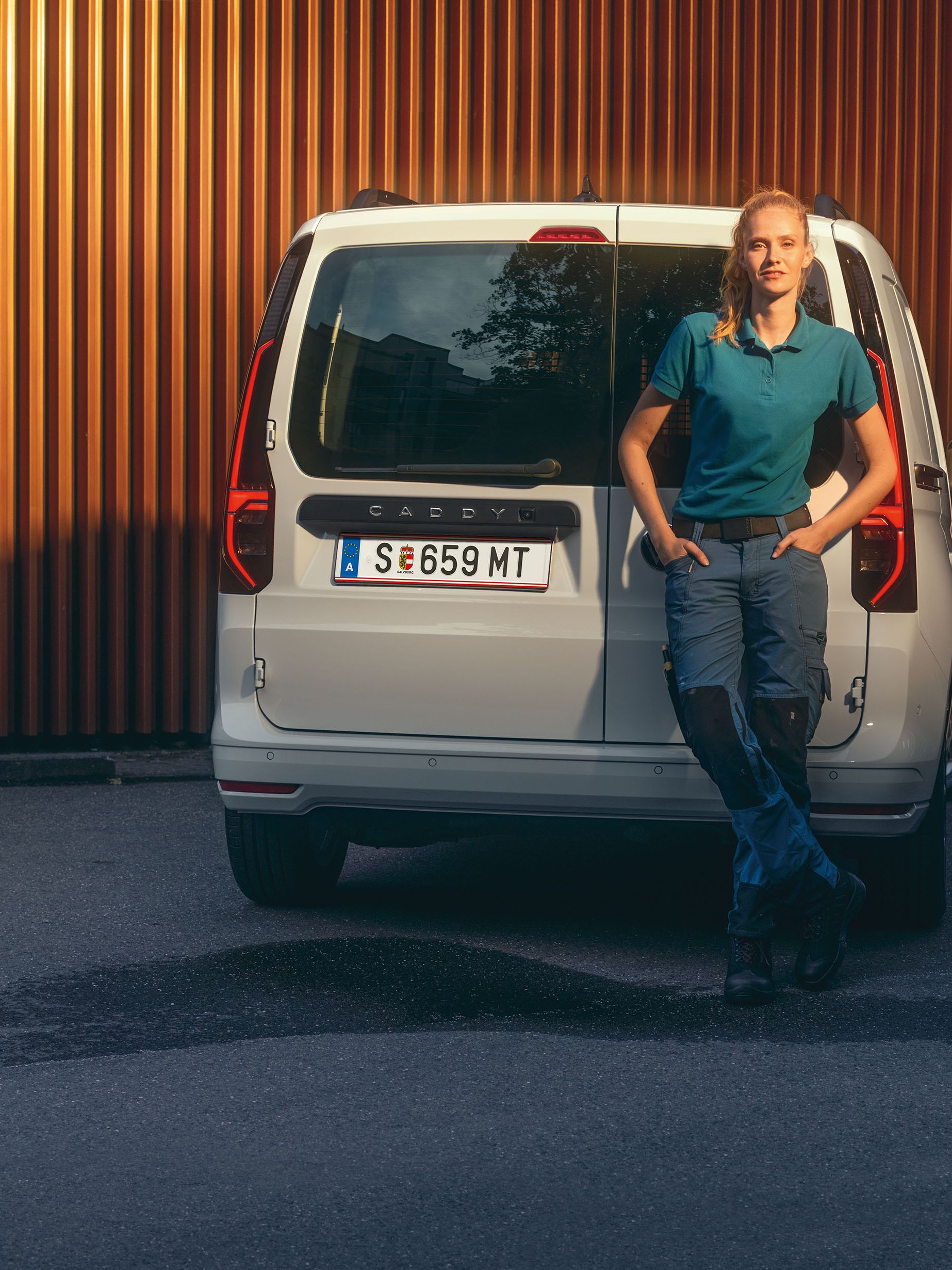 Eine Frau lehnt am Heck eines weißen VW Caddy Cargo.