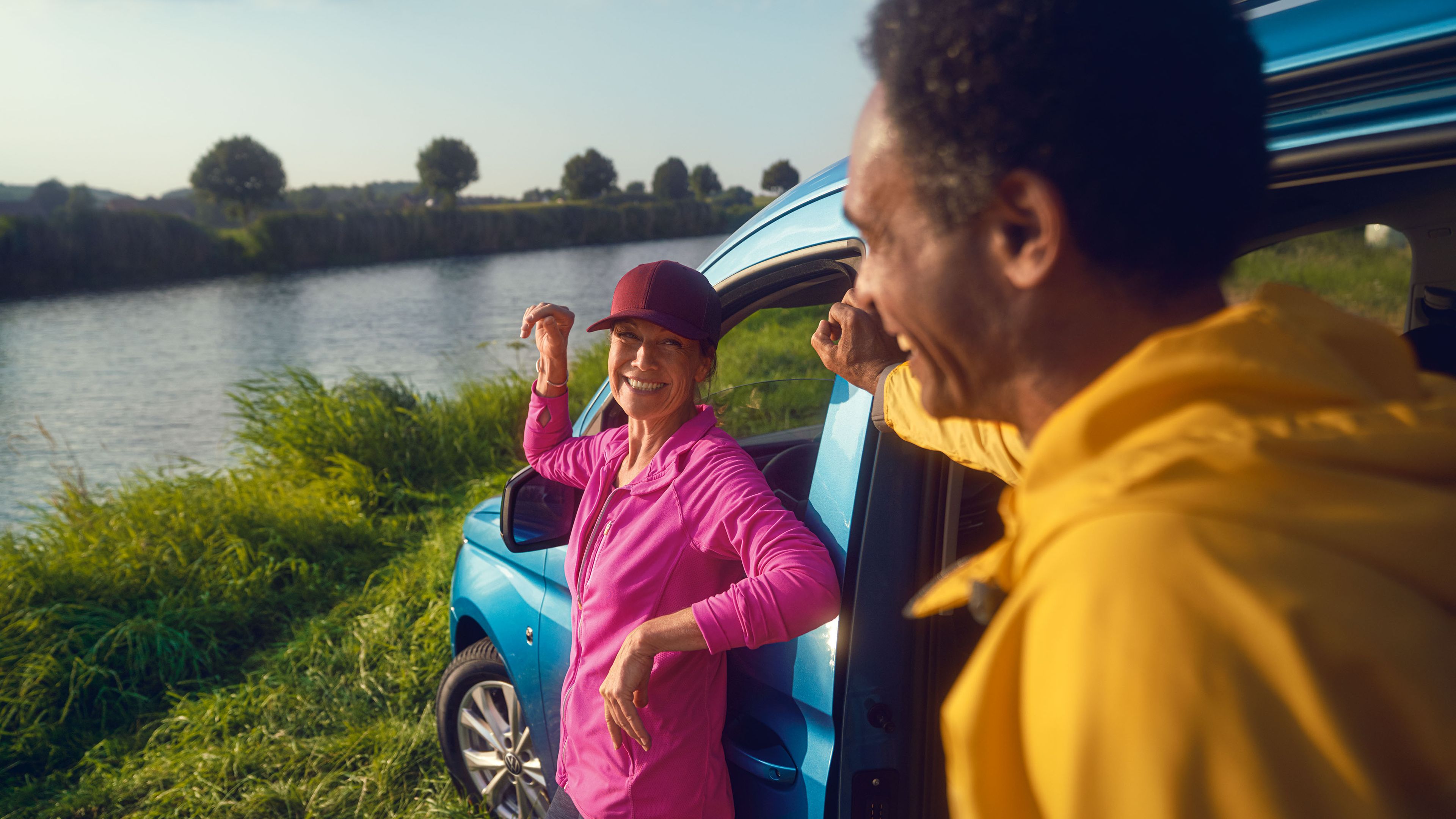 Ein Mann und eine Frau steht mit einem VW Caddy auf der Wiese eines Flussufers.