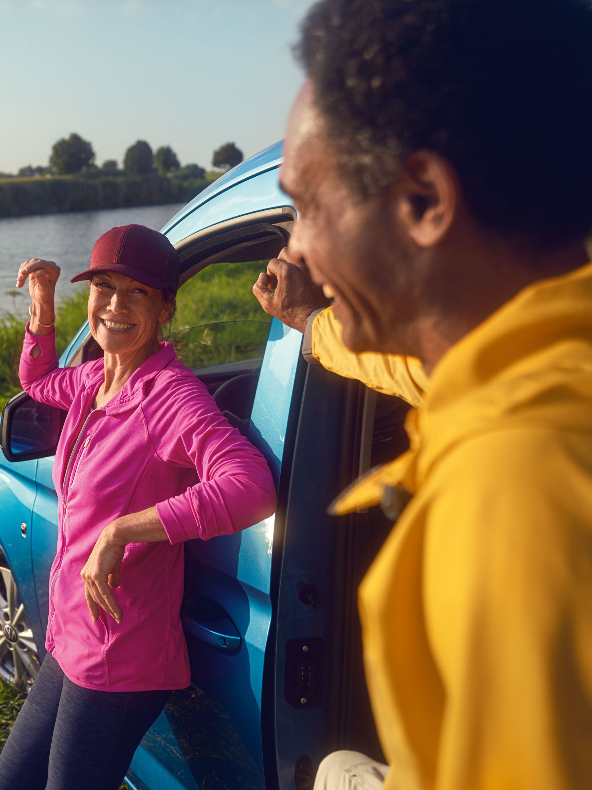 Ein Mann und eine Frau steht mit einem VW Caddy auf der Wiese eines Flussufers.