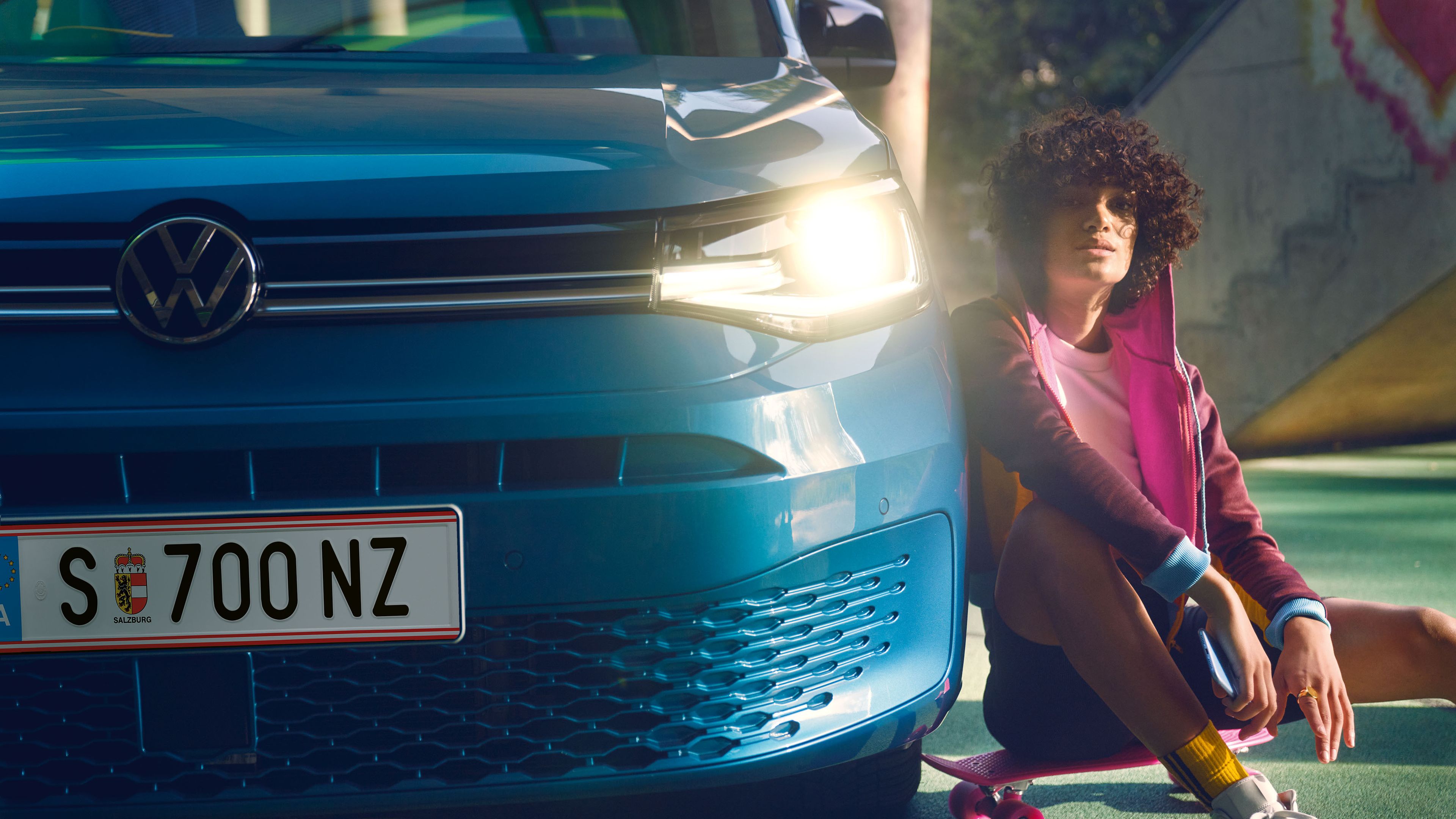 EinTeenager sitzt auf seinem Skateboard neben einem VW Caddy.